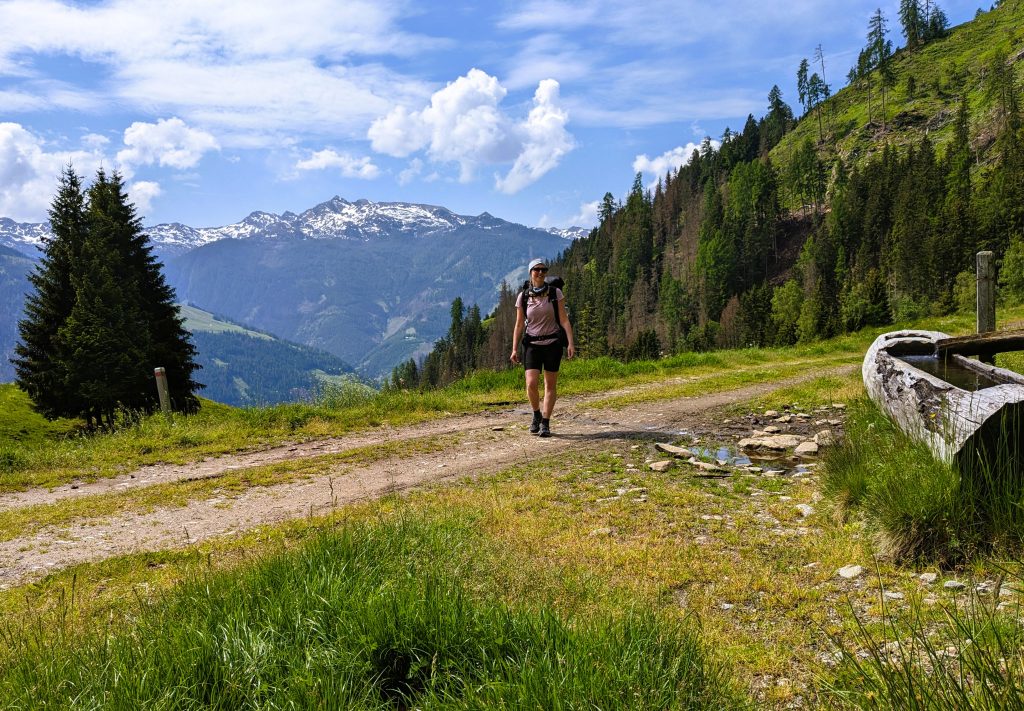 Alpe-Adria-Trail Weitwanderung Bergpanorama mit Holzbrunnen junge Wanderin mit Rucksack